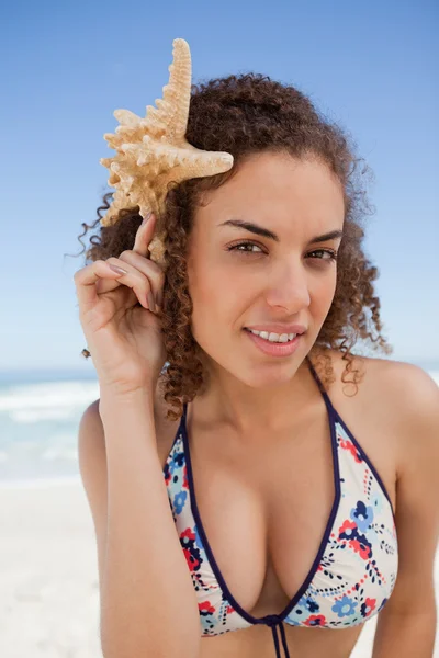Jovem mulher atraente segurando uma estrela do mar ao lado de sua cabeça — Fotografia de Stock
