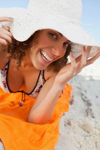 Young smiling woman holding her hat brim while lying down — Stock Photo, Image