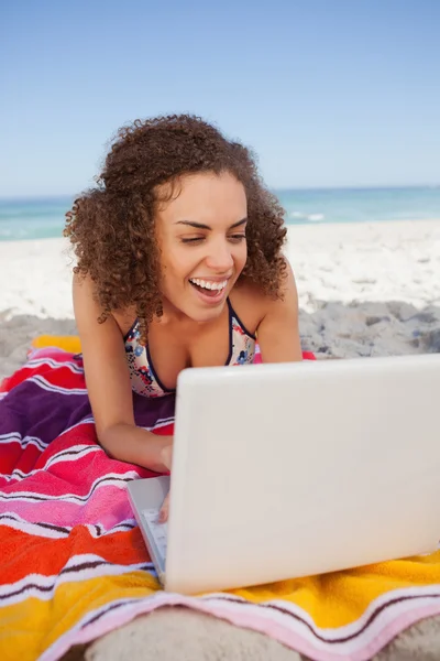 年轻有魅力的女人在笑的同时在海滩上使用便携式计算机 — 图库照片