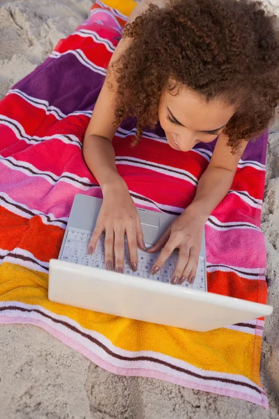 Giovane donna sorridente sdraiata sul suo telo da spiaggia mentre digita su di lei — Foto Stock
