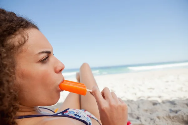 Jeune femme attrayante manger une glace éclatante sur la plage — Photo