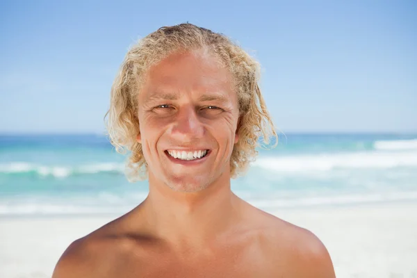 Młody człowiek uśmiechający się stojąc na plaży — Zdjęcie stockowe
