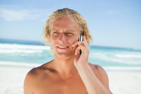 Sarışın adam bea üzerinde duran cep telefonuna konuşuyor — Stok fotoğraf