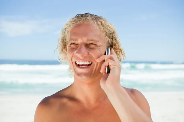 Усміхнений чоловік використовує свій мобільний телефон, стоячи на пляжі — стокове фото