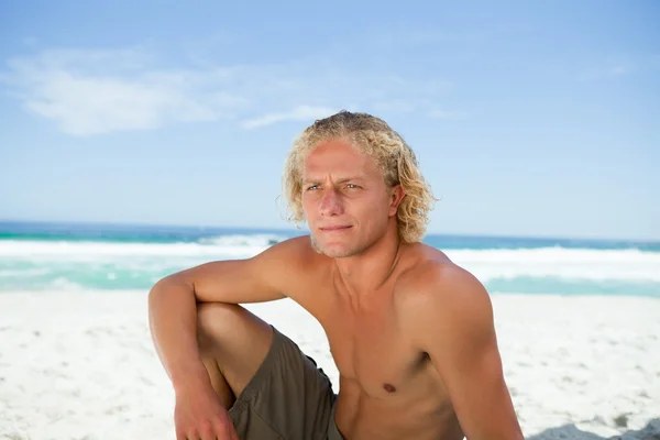 Uomo serio seduto sulla spiaggia mentre guarda verso il lato — Foto Stock