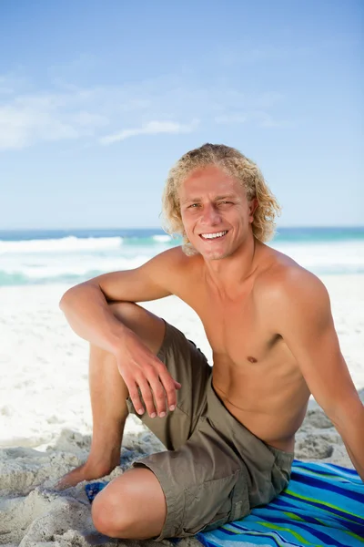 微笑男子坐上他的沙滩巾同时看了就来了 — 图库照片