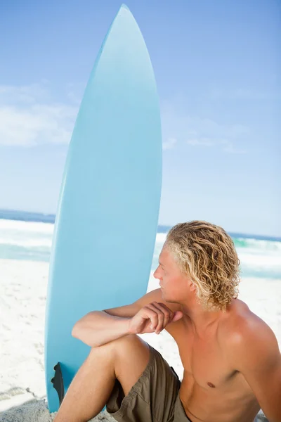 Серйозний блондинка сидить на пляжі зі своєю дошкою для серфінгу поруч — стокове фото
