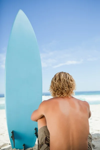 Blond man sitter på stranden med armarna runt hans ben — Stockfoto