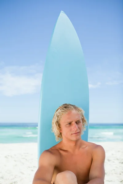 Homme blond sérieux assis devant sa planche de surf — Photo