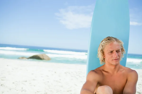 Biondo uomo seduto di fronte alla sua tavola da surf mentre cerca towar — Foto Stock