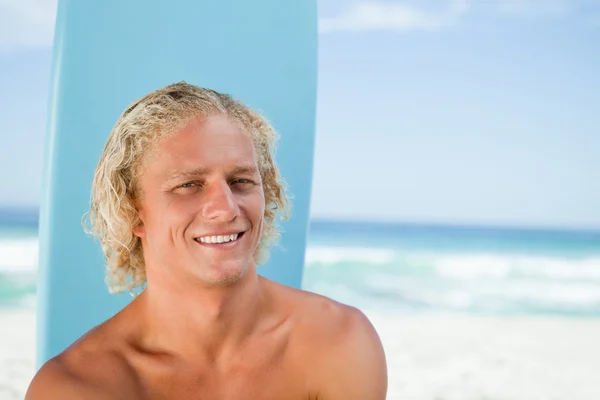 Jovem sorridente sentado em frente ao oceano com sua surfboa — Fotografia de Stock