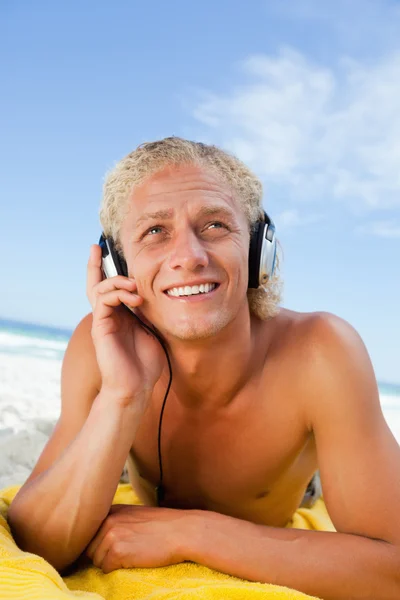Homem sorridente deitado na praia enquanto ouve música — Fotografia de Stock
