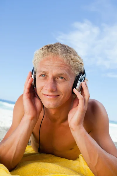 Jovem sorridente deitado em sua toalha de praia amarela enquanto escuta — Fotografia de Stock