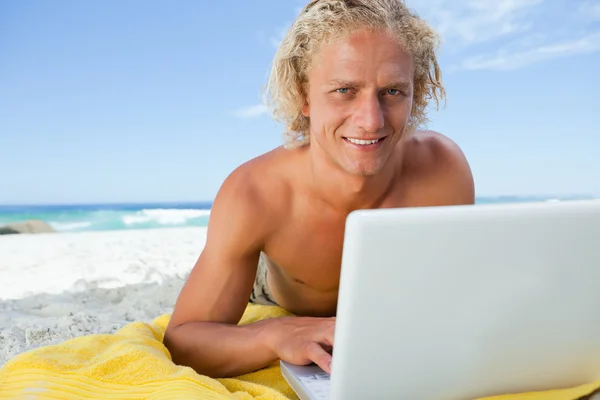 Χαμογελώντας ξανθιά άνθρωπος που βρίσκεται στην παραλία κατά τη χρήση του φορητού υπολογιστή — Φωτογραφία Αρχείου