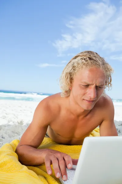 金发碧眼的人躺在海滩上同时使用他的笔记本电脑中非常 c — 图库照片