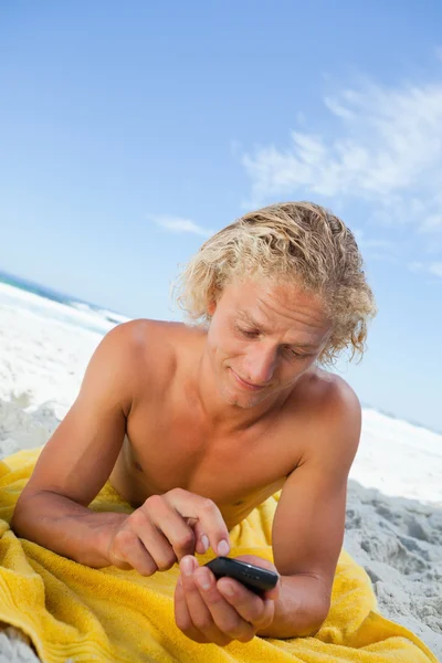 Giovane uomo biondo che invia un messaggio con il suo cellulare mentre prende il sole — Foto Stock