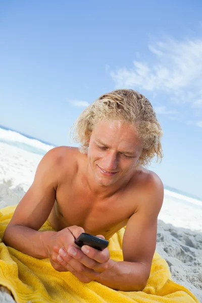 Uomo biondo sdraiato sul suo telo da spiaggia durante l'invio di un messaggio — Foto Stock