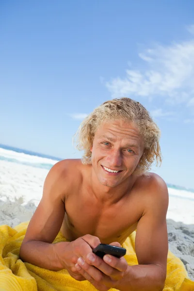 微笑着金发碧眼的人在沙滩上享受日光浴的同时发送文本 — 图库照片