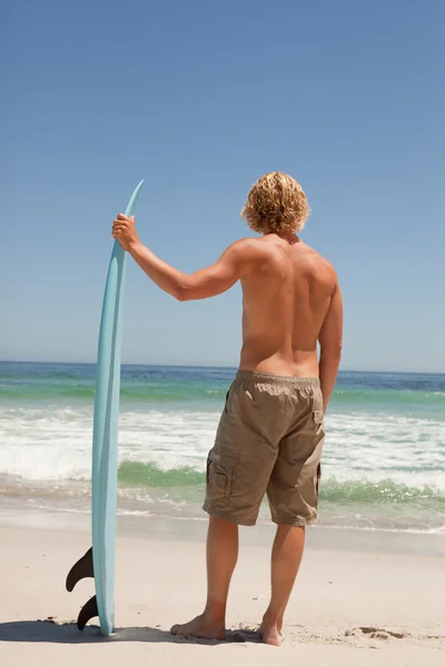 Jovem loira segurando sua prancha de surf na frente do oceano — Fotografia de Stock