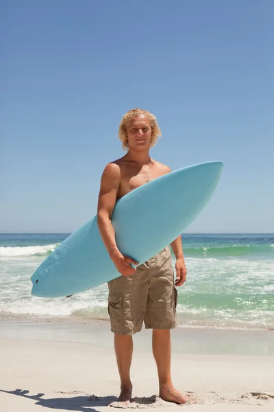 Blond man med sin surfbräda stående framför den — Stockfoto