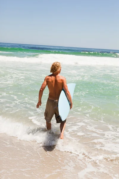Młody człowiek blondynka, trzymając jego deskę surfingową podczas spaceru w wate — Zdjęcie stockowe