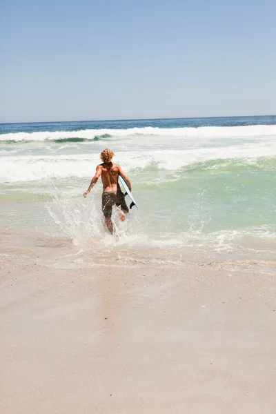 Młody blond człowiek działa w wodzie z jego deskę surfingową — Zdjęcie stockowe