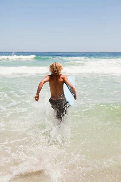 Fiatal szőke férfi gazdaság a kék szörf, miközben fut a — Stock Fotó