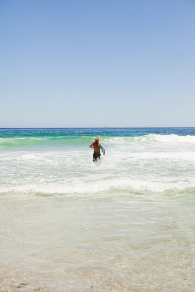 Bakifrån av en blond man kör i vattnet med sin surfboar — Stockfoto