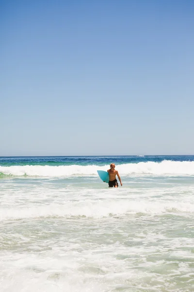 Młody człowiek blondynka, chodzenie w wodzie z jego deskę surfingową — Zdjęcie stockowe