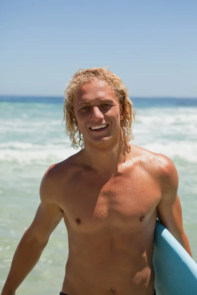 Улыбающийся человек стоит в воде, держа доску для сёрфинга — стоковое фото