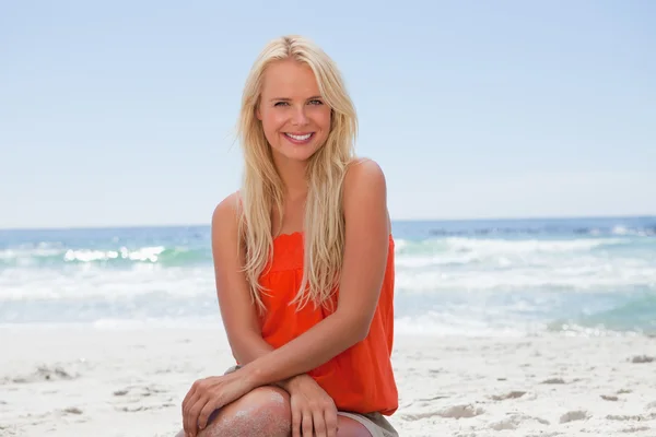 Usměvavá mladá žena vsedě na pobřeží oceánu — Stock fotografie