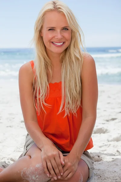 Jonge lachende blonde vrouw zittend op het strand — Stockfoto