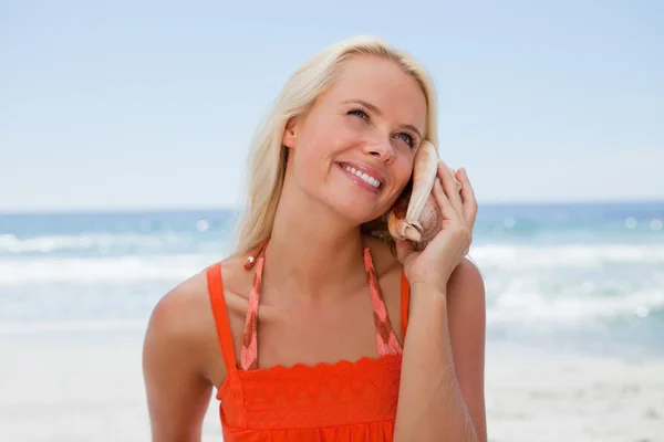 Jonge blonde vrouw luisteren naar het geluid van de zee via een s — Stockfoto