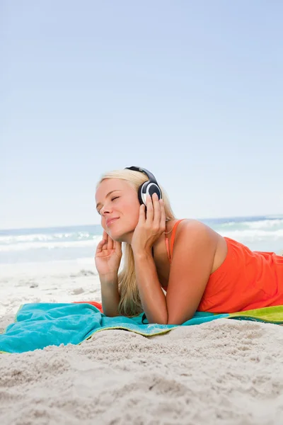 En omtenksom ung kvinne som ligger på stranden mens hun hører på mus. – stockfoto