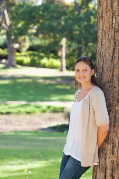En smilende kvinne lener seg mot et tre – stockfoto