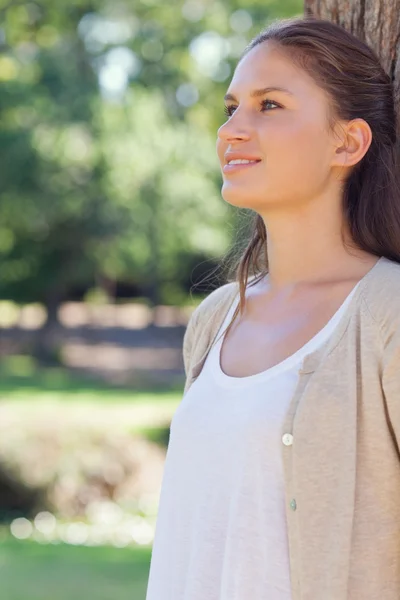 Smiling woman leaning against a tree in the park — Stock Photo, Image