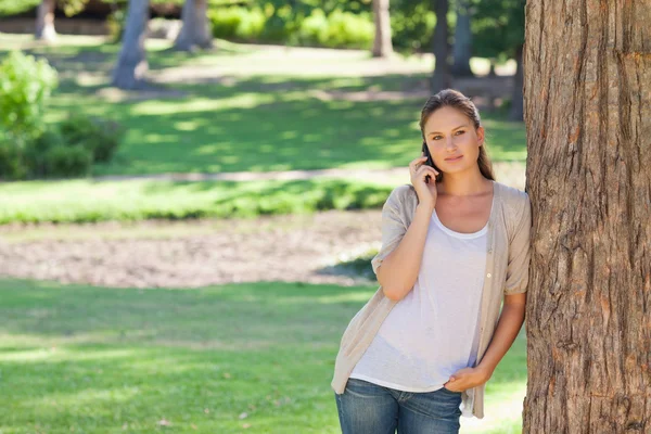 Kadın telefonda karşı bir ağaca yaslanmış — Stok fotoğraf