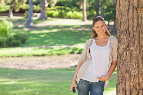 Woman with a cellphone leaning against a tree — Stock Photo, Image