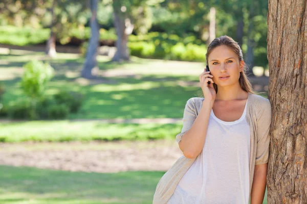 Woman on the cellphone leaning against a tree — Stock Photo, Image