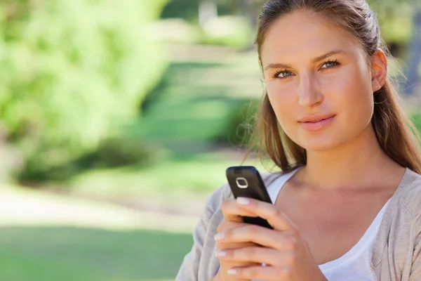 Close up of woman holding her mobile phone in the park — Stock Photo, Image