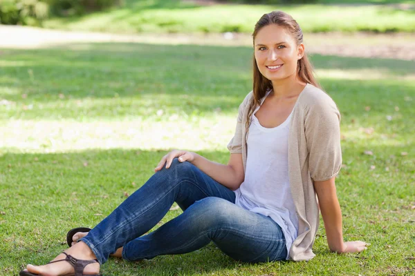 芝生の上に座っている女性の笑みを浮かべてください。 — ストック写真