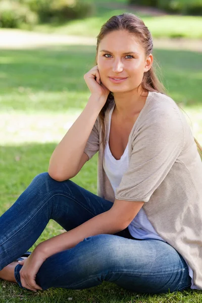 Задумчивая женщина, сидящая на газоне — стоковое фото