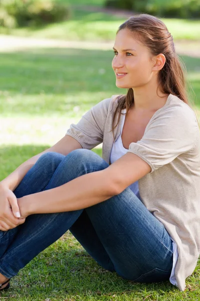 Vista lateral de uma mulher sentada no gramado — Fotografia de Stock