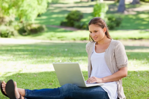 Женщина, сидящая на газоне со своим ноутбуком — стоковое фото
