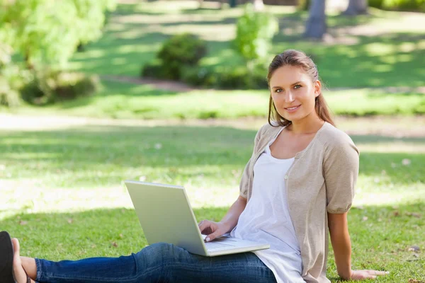 她坐在草坪上的笔记本电脑的女人 — 图库照片