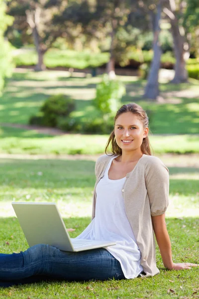 Donna sorridente con il suo computer portatile seduto nel parco — Foto Stock