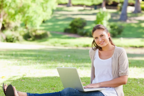 Улыбающаяся женщина сидит на траве со своим ноутбуком — стоковое фото