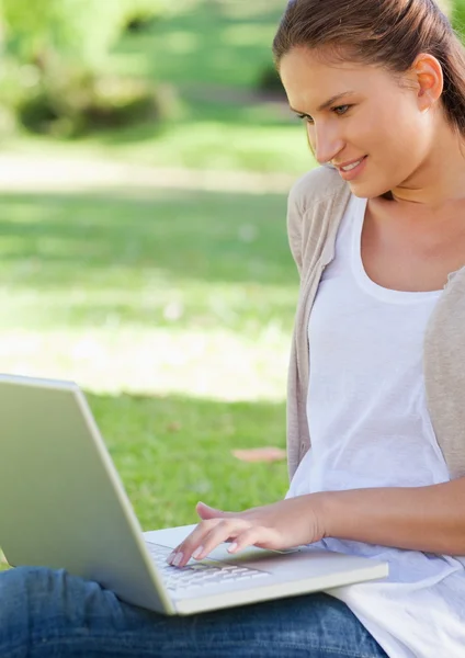 Χαμογελαστή γυναίκα χρησιμοποιώντας το laptop, ενώ κάθεται στο γρασίδι — Φωτογραφία Αρχείου