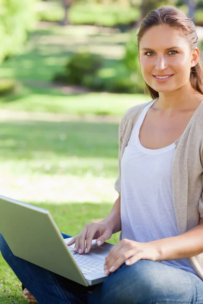 Улыбающаяся женщина, работающая над ноутбуком в парке — стоковое фото