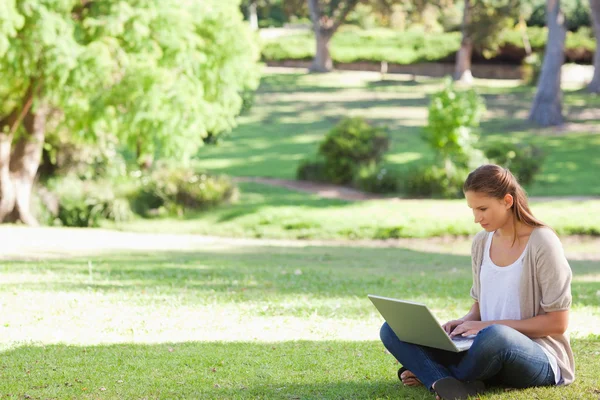 Kobieta siedzi na trawniku, działa na jej notatnik — Zdjęcie stockowe